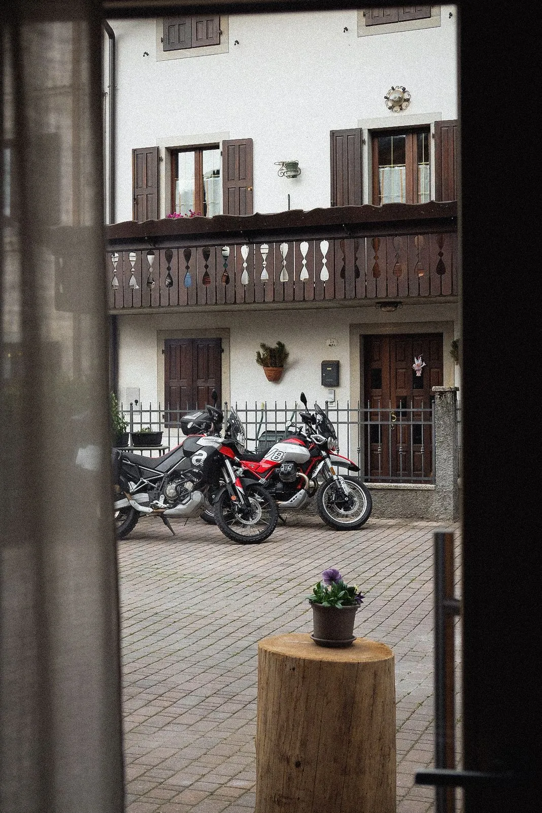 View through a doorway of two adventure bikes parked in a stone courtyard outside an Italian house