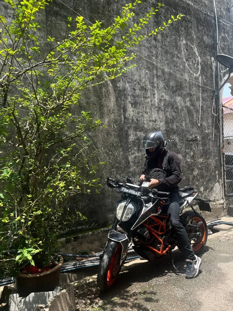Helmeted rider seated on an orange KTM naked bike in a narrow alley beside a concrete wall