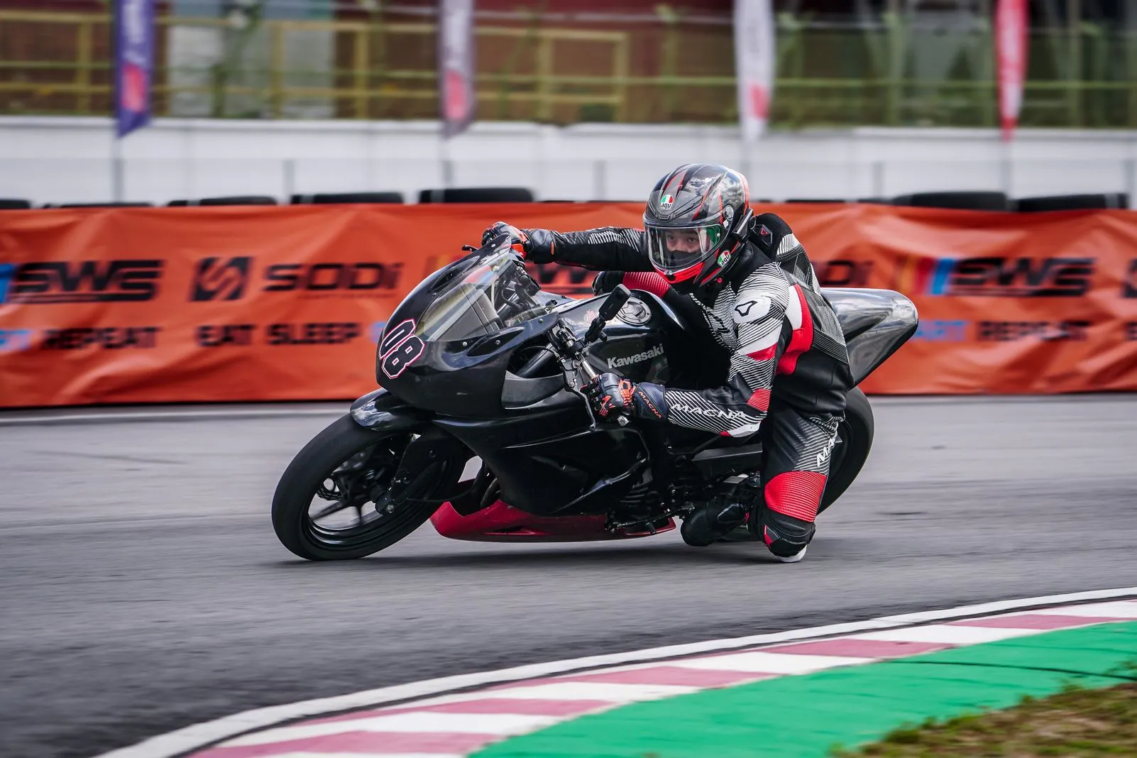 Rider in black and white leathers leaned hard into a corner on a black Kawasaki race bike