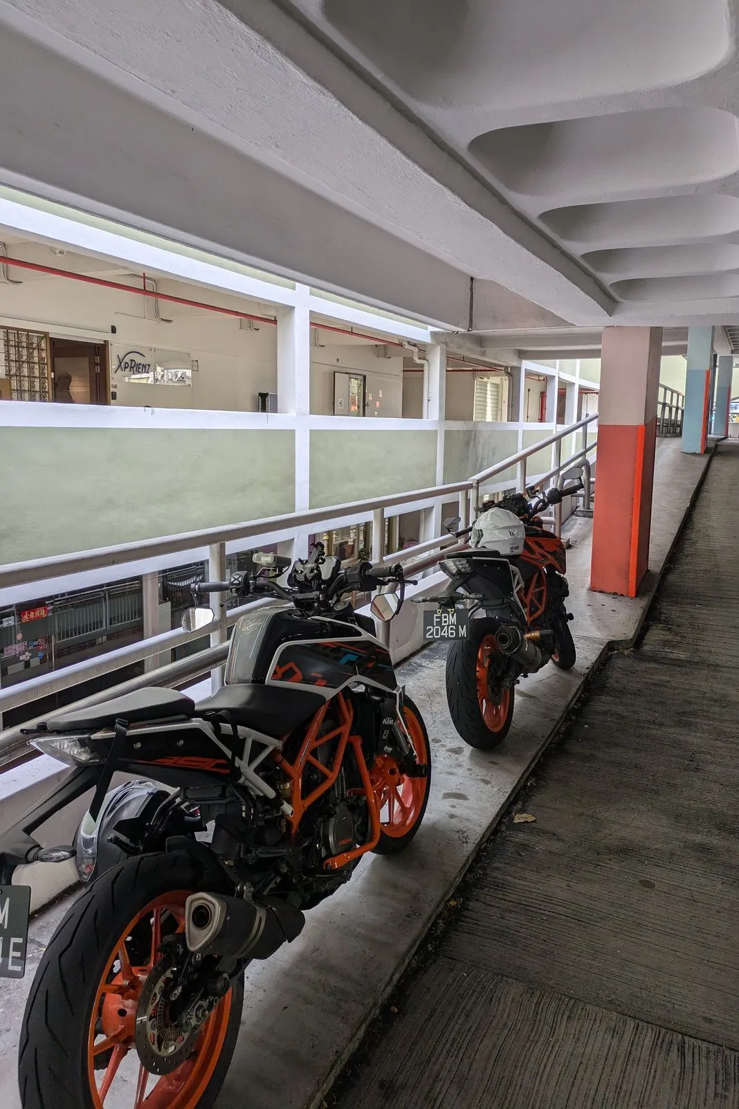Two orange-and-black KTM Duke naked bikes parked along a covered walkway railing