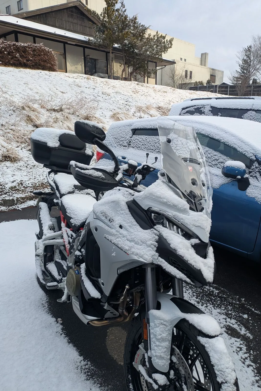 Ducati Multistrada buried under fresh snow next to a snow-covered parked car