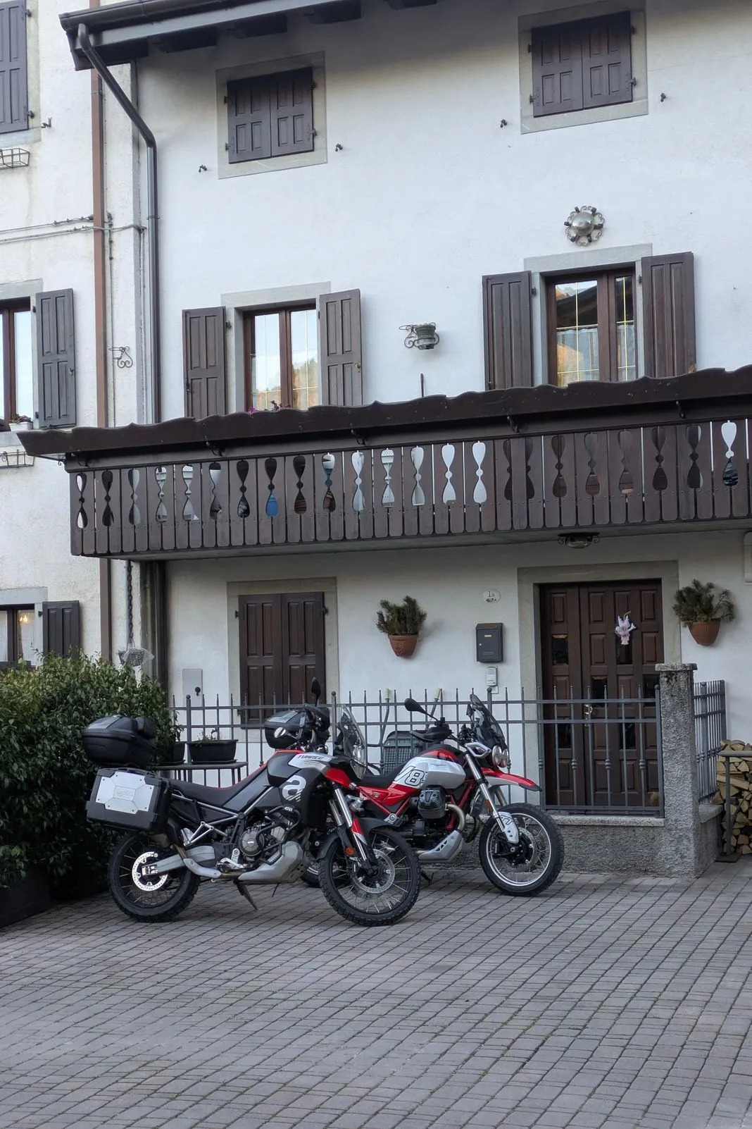 Two adventure bikes parked outside an alpine house with wooden shutters and a carved balcony