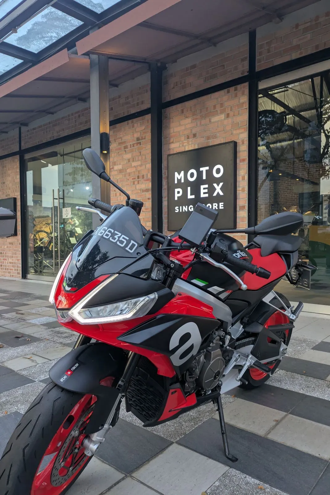 Red and black Aprilia sportbike parked outside the Motoplex Singapore storefront