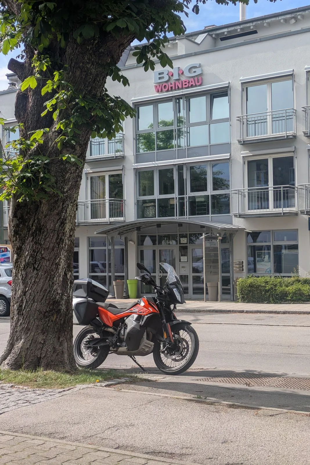 Orange and black KTM adventure bike with side cases parked under a tree by an apartment building