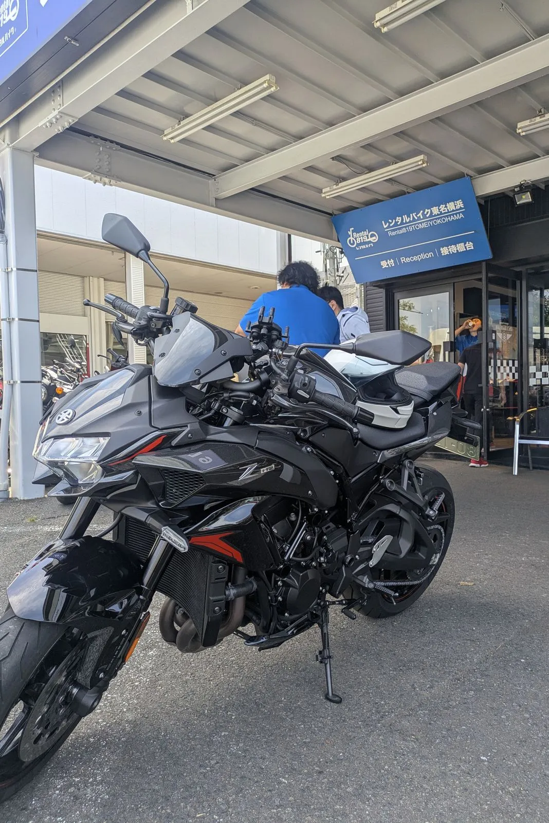 Black naked sport bike parked outside a rental bike shop with Japanese signage