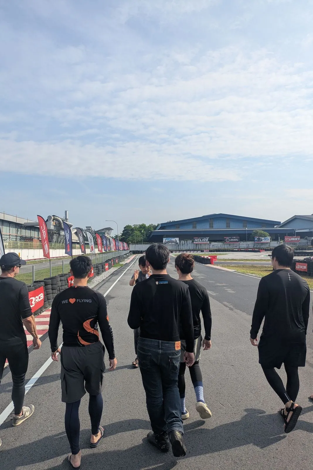 Group of riders in matching black rash guards walking down pit lane at a race track