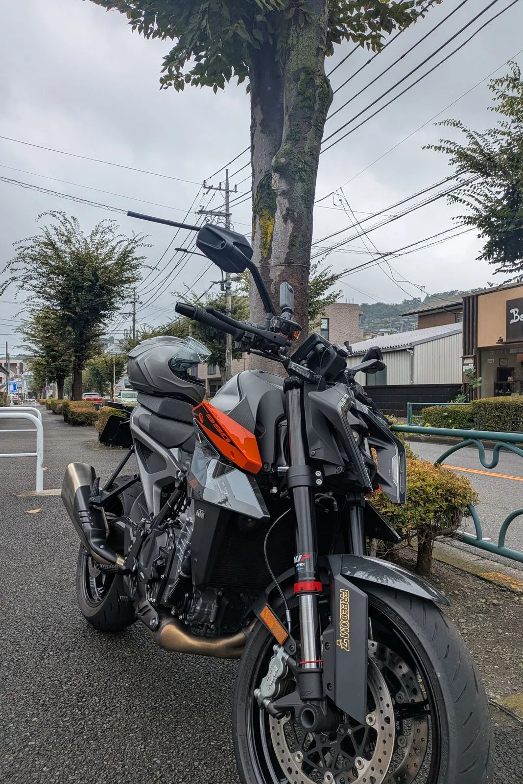 KTM naked bike parked streetside under a tree with a helmet resting on the seat