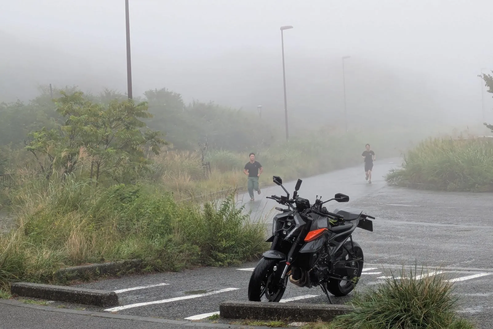 Black KTM naked bike parked on a foggy road as two joggers run past in the mist