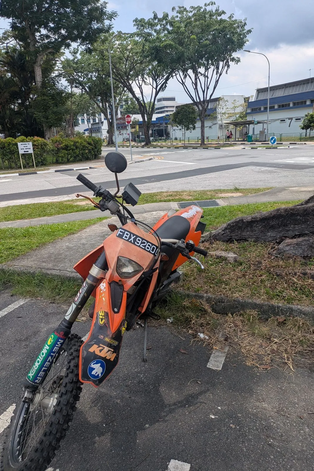 Orange KTM enduro bike parked on a curb near a road junction on an overcast day