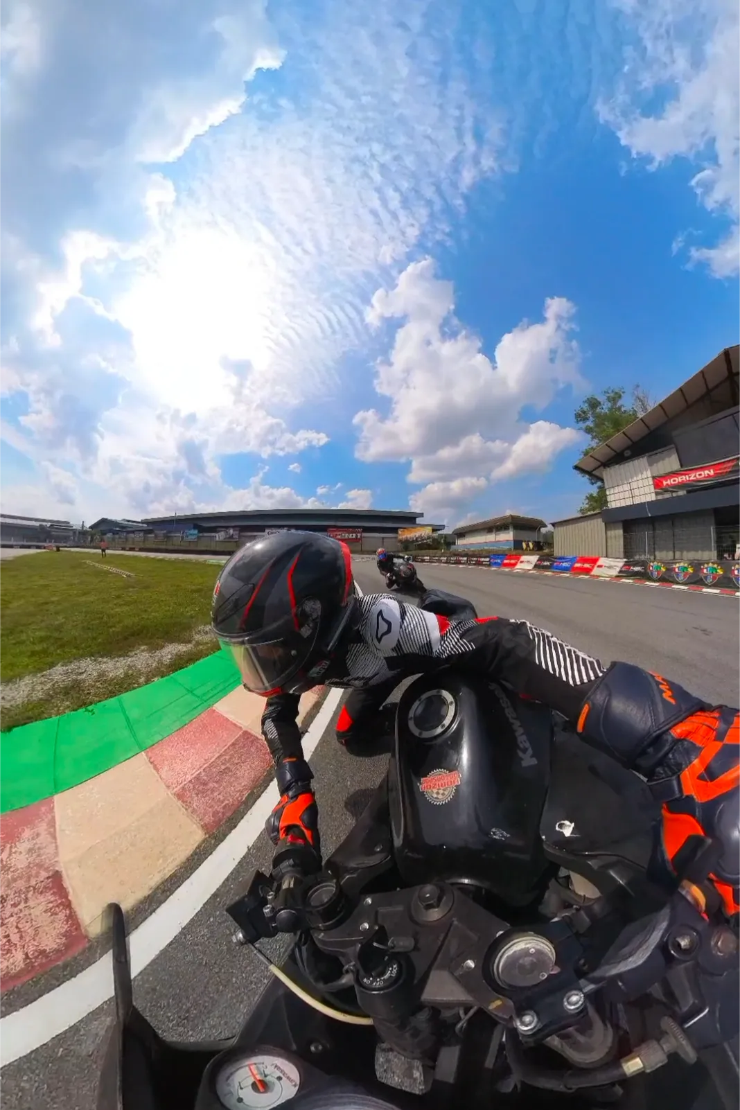 Chest-cam view leaning into a track corner on painted curbing under a wide cloudy sky