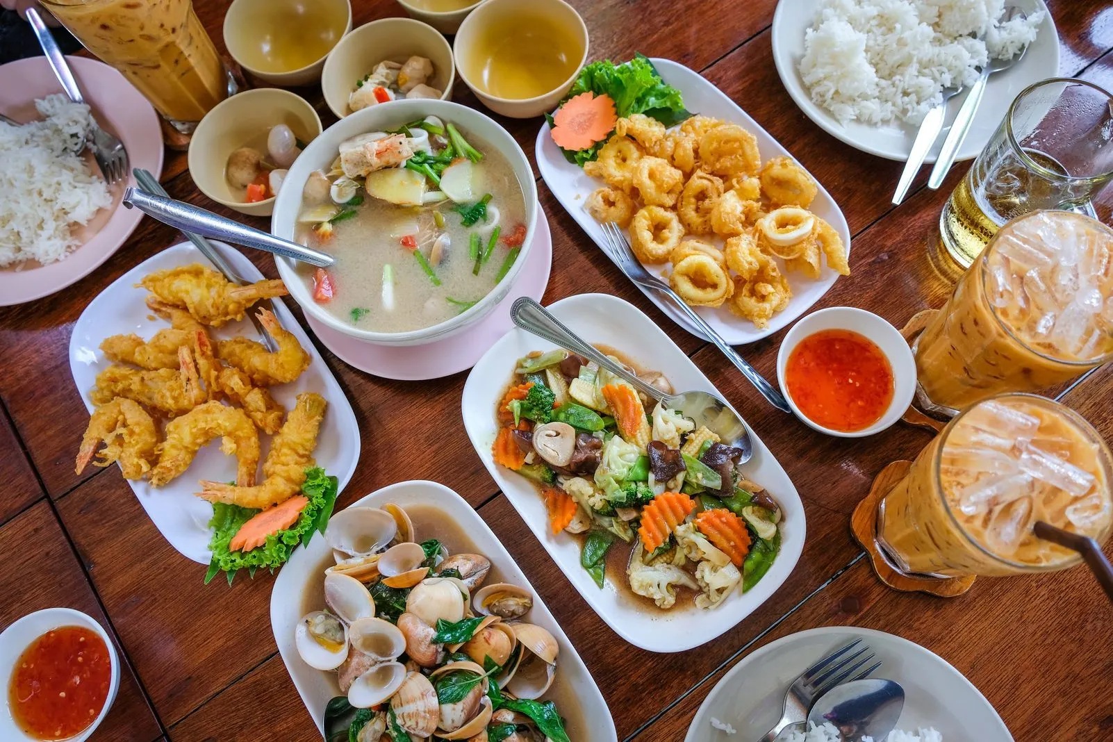 Overhead view of a Thai seafood spread with soup, fried shrimp, calamari, and clams