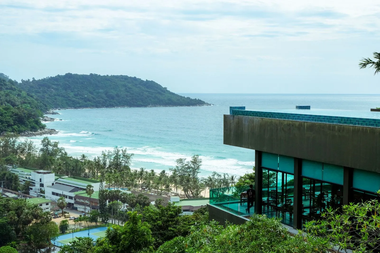Clifftop restaurant overlooking a bay with an infinity pool edge and tennis courts below