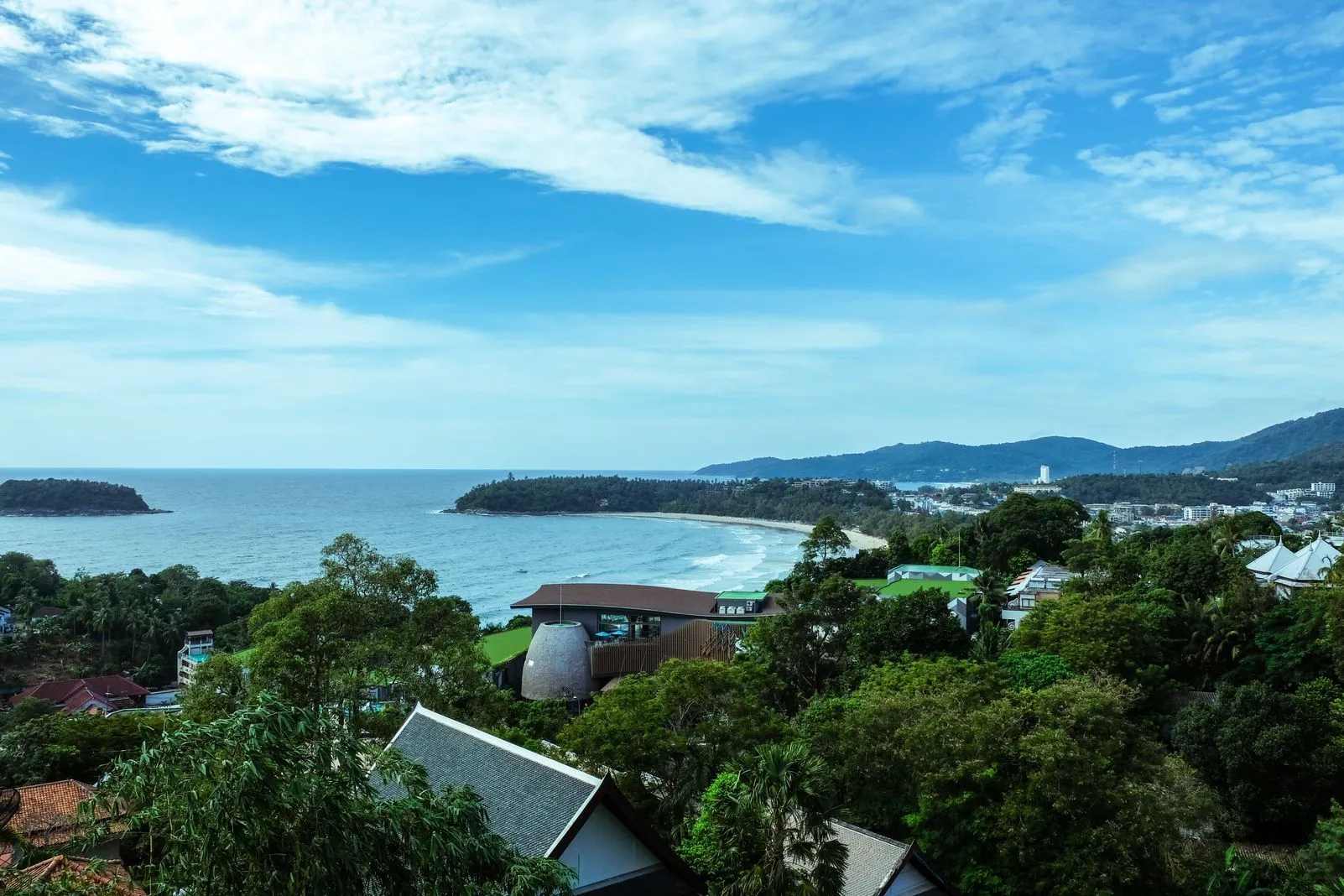 Elevated view of a curving coastline with sea, a wooded headland, and hillside buildings