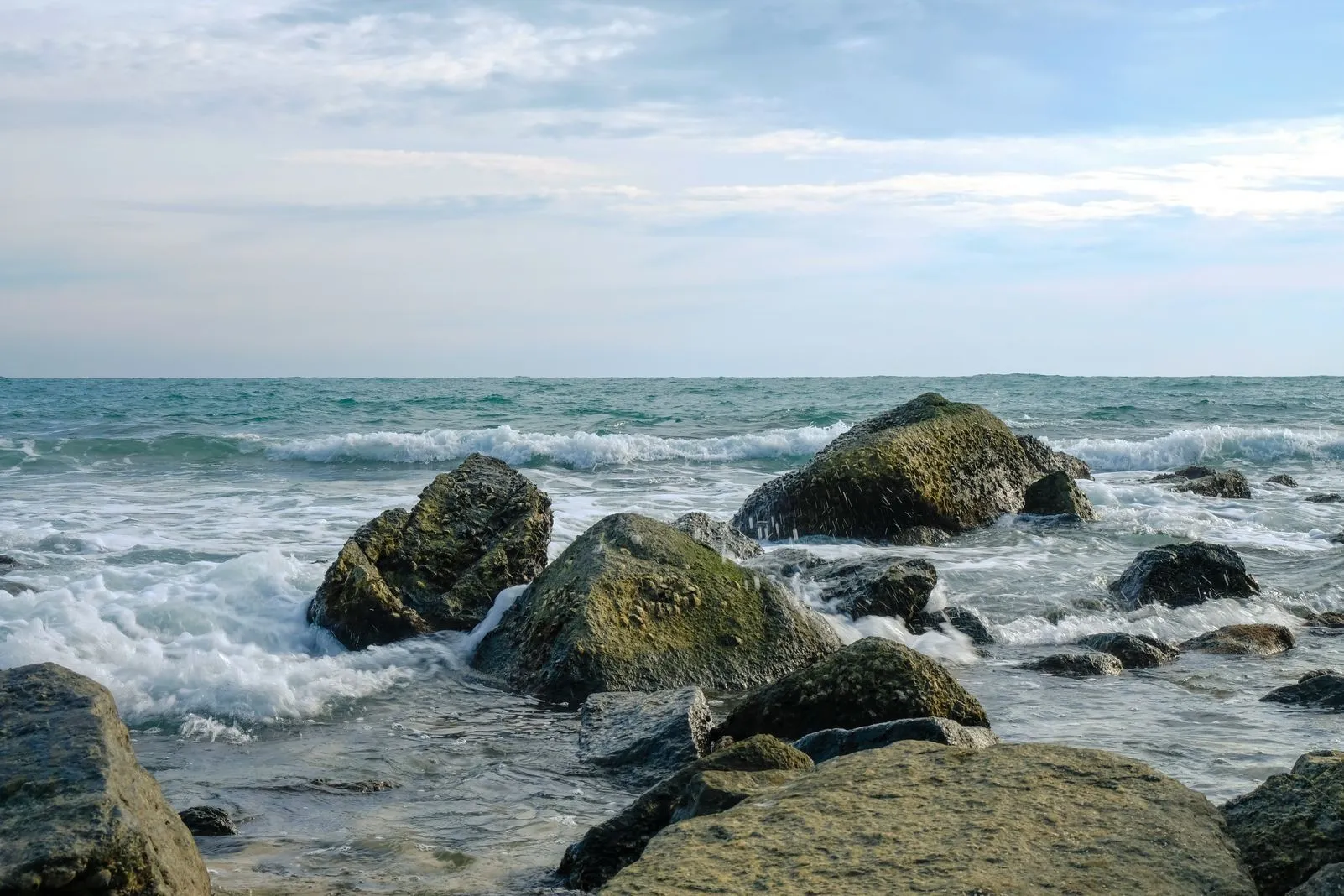Waves breaking over moss-covered rocks along the shoreline