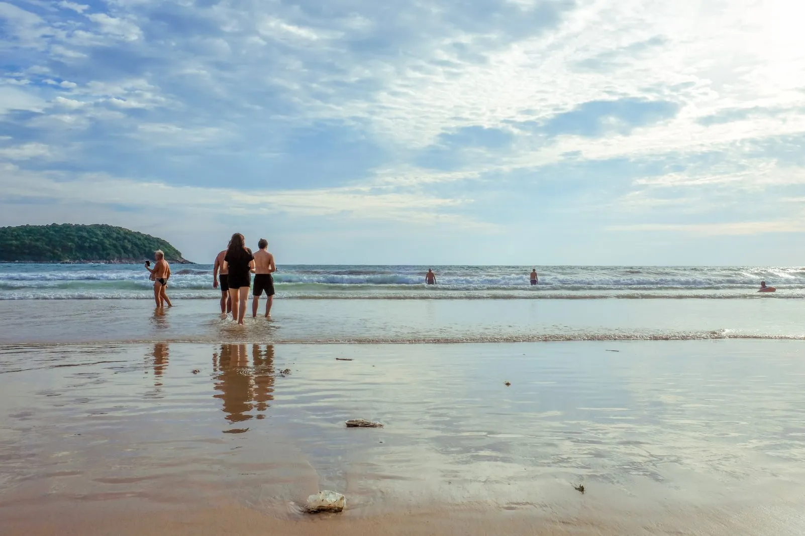 People wading into gentle surf at sunset, their reflections in the wet sand