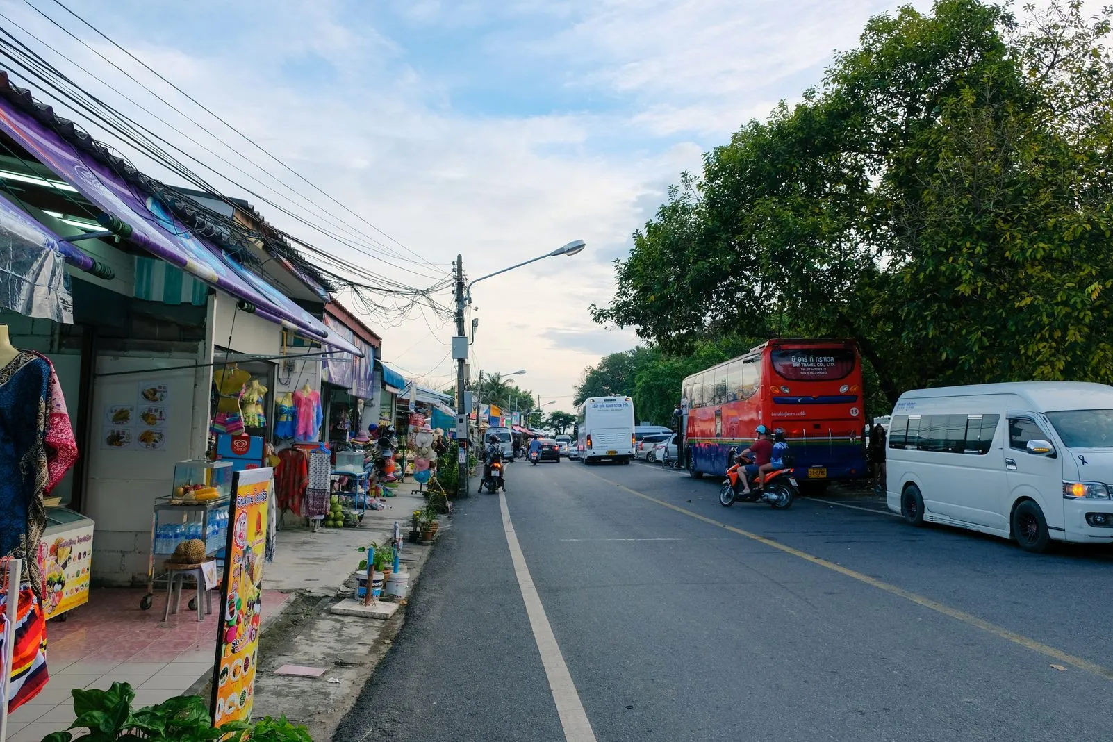 Street lined with shops and stalls, a red tour bus and motorbikes passing at dusk