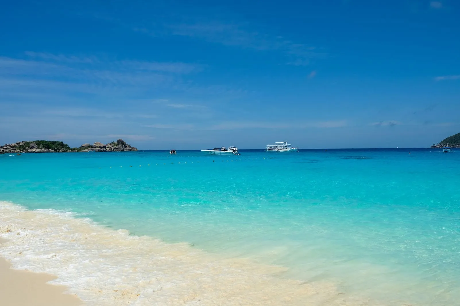 Clear turquoise water and white sand with tour boats anchored offshore