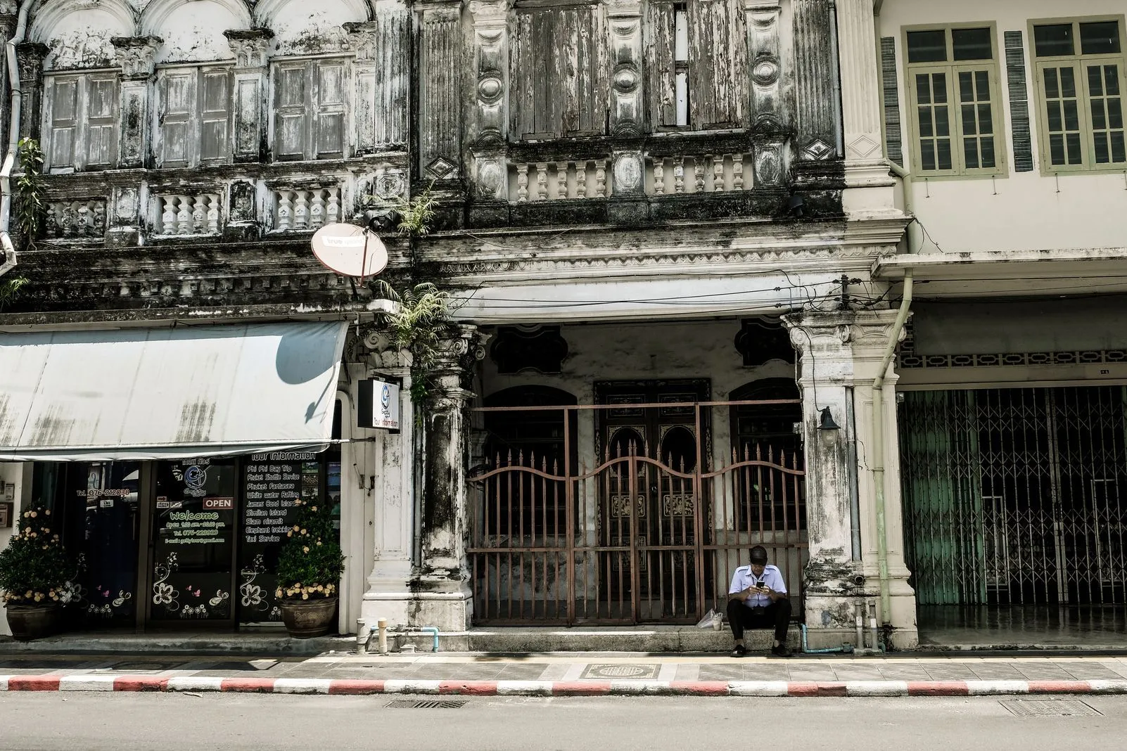 Weathered Sino-Portuguese shophouse facade with a security guard seated outside