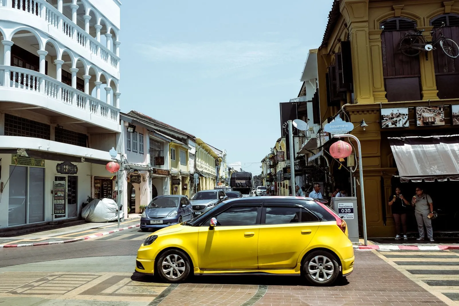 Yellow hatchback at an intersection lined with colorful Sino-Portuguese buildings and red lanterns