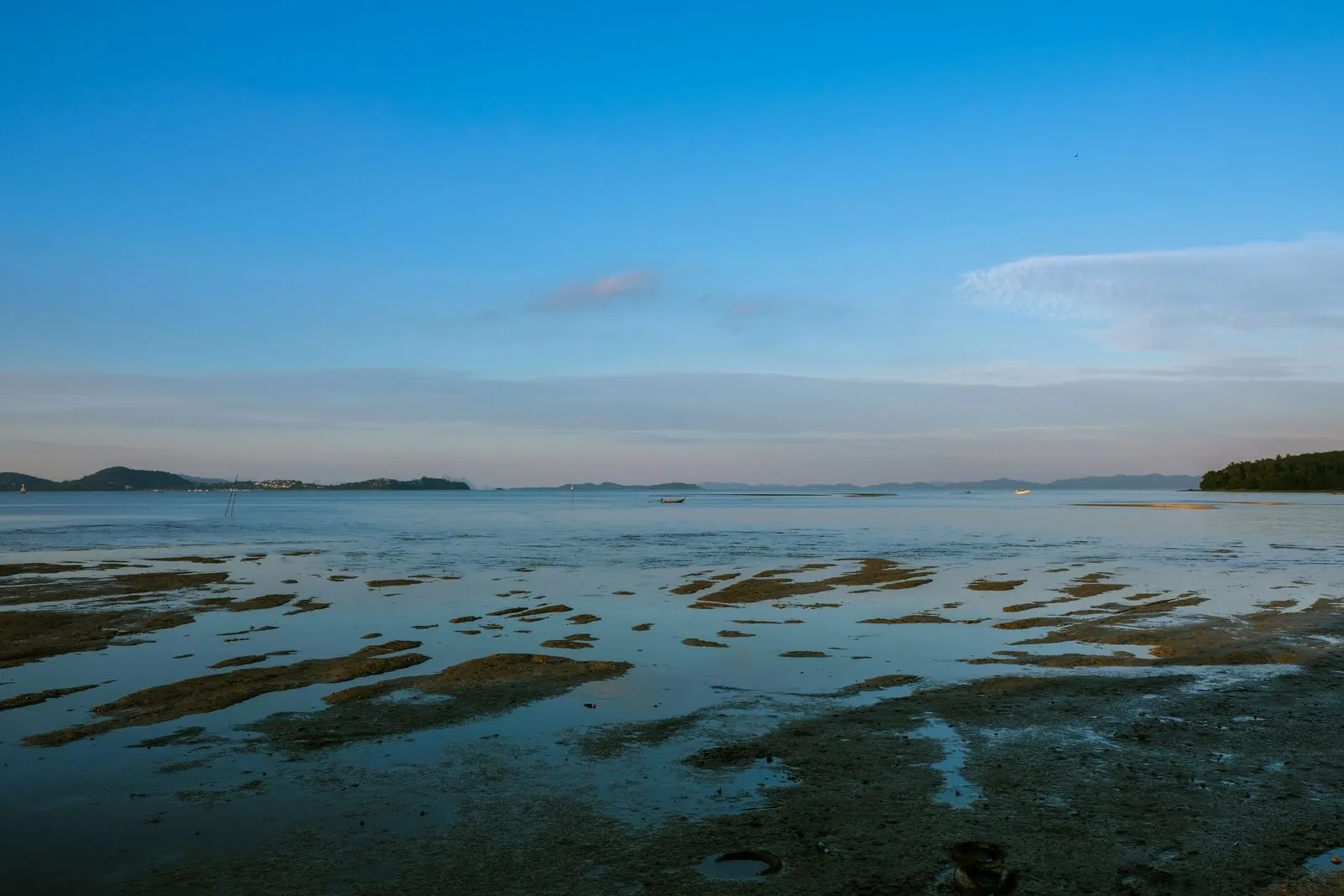 Wide tidal flats and calm water at dusk with distant boats and hills