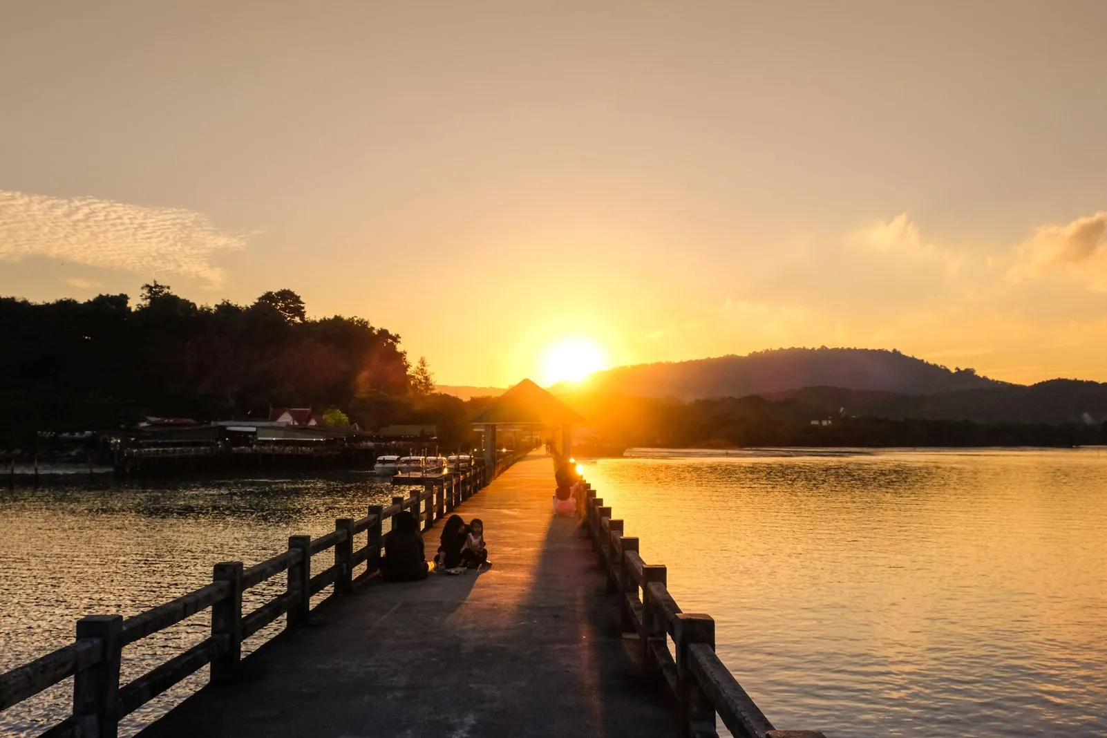 Golden sunset over a bay with people walking along a long pier