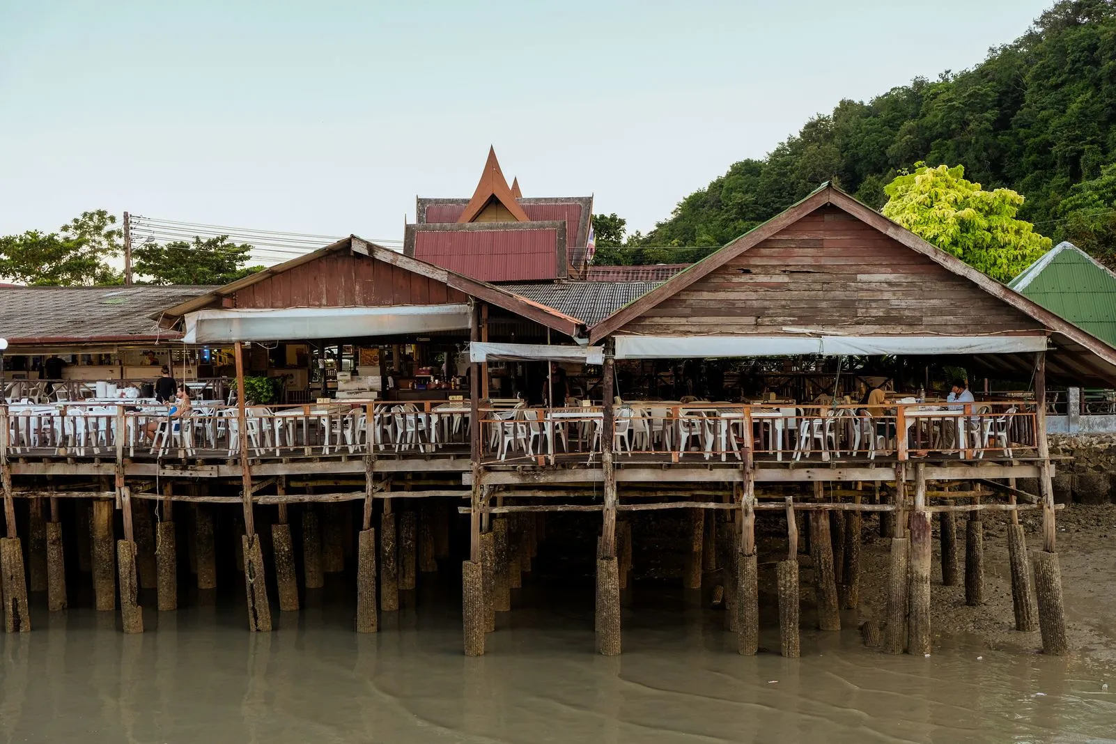 Waterfront restaurant on stilts with rows of tables overlooking muddy tidal water