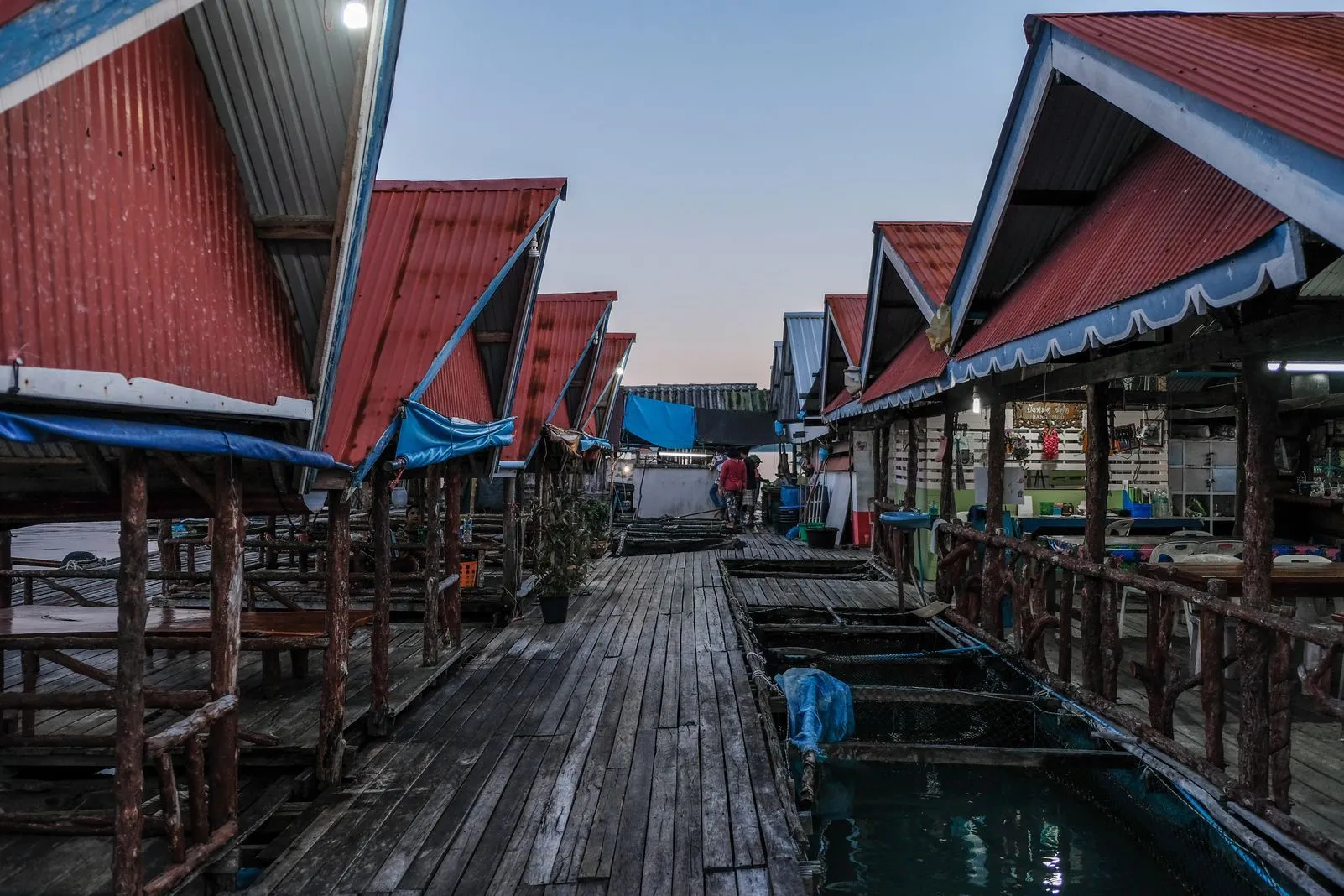 Row of red-roofed floating huts along a wooden boardwalk at dusk
