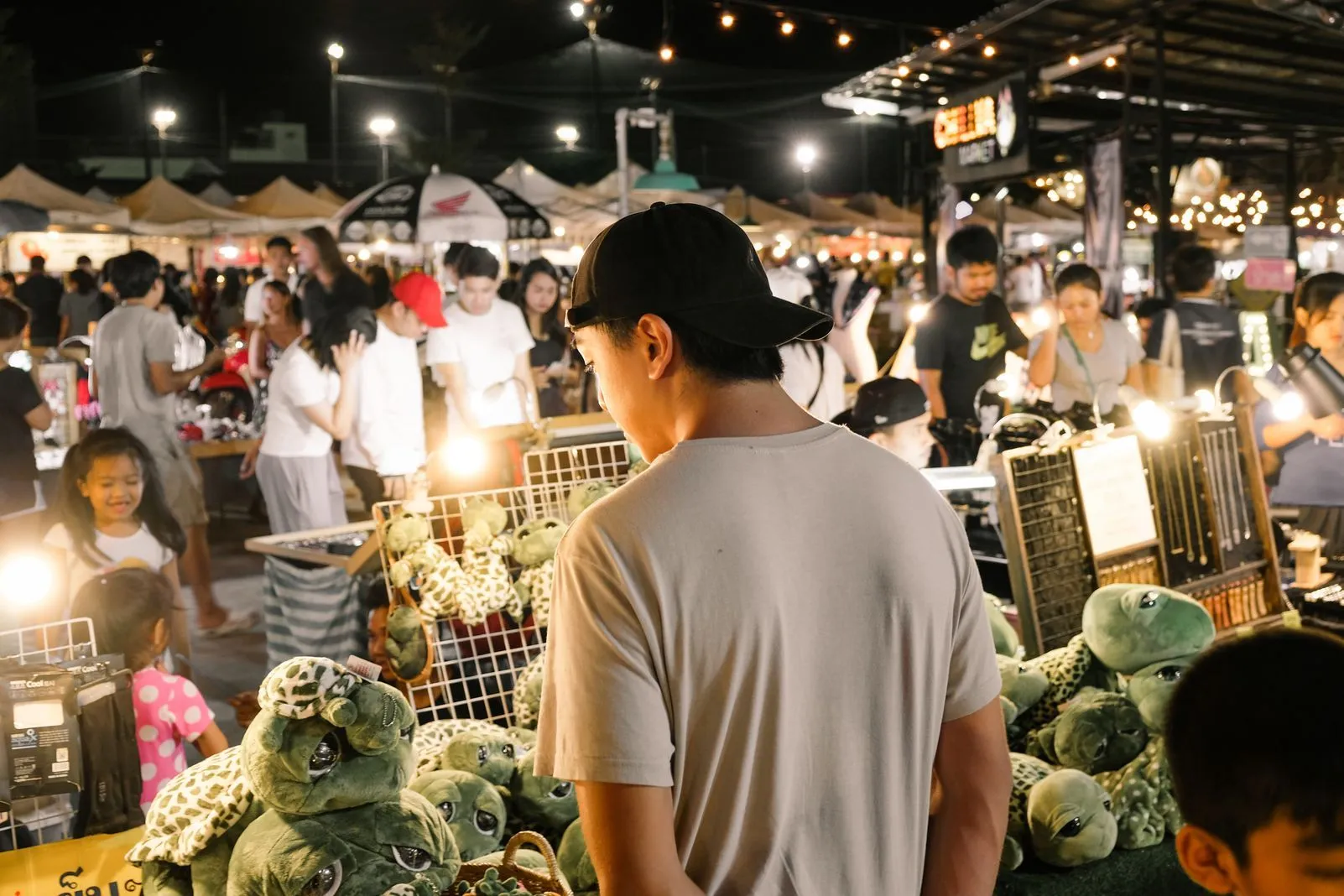 Person browsing stuffed turtle toys at a crowded night market stall