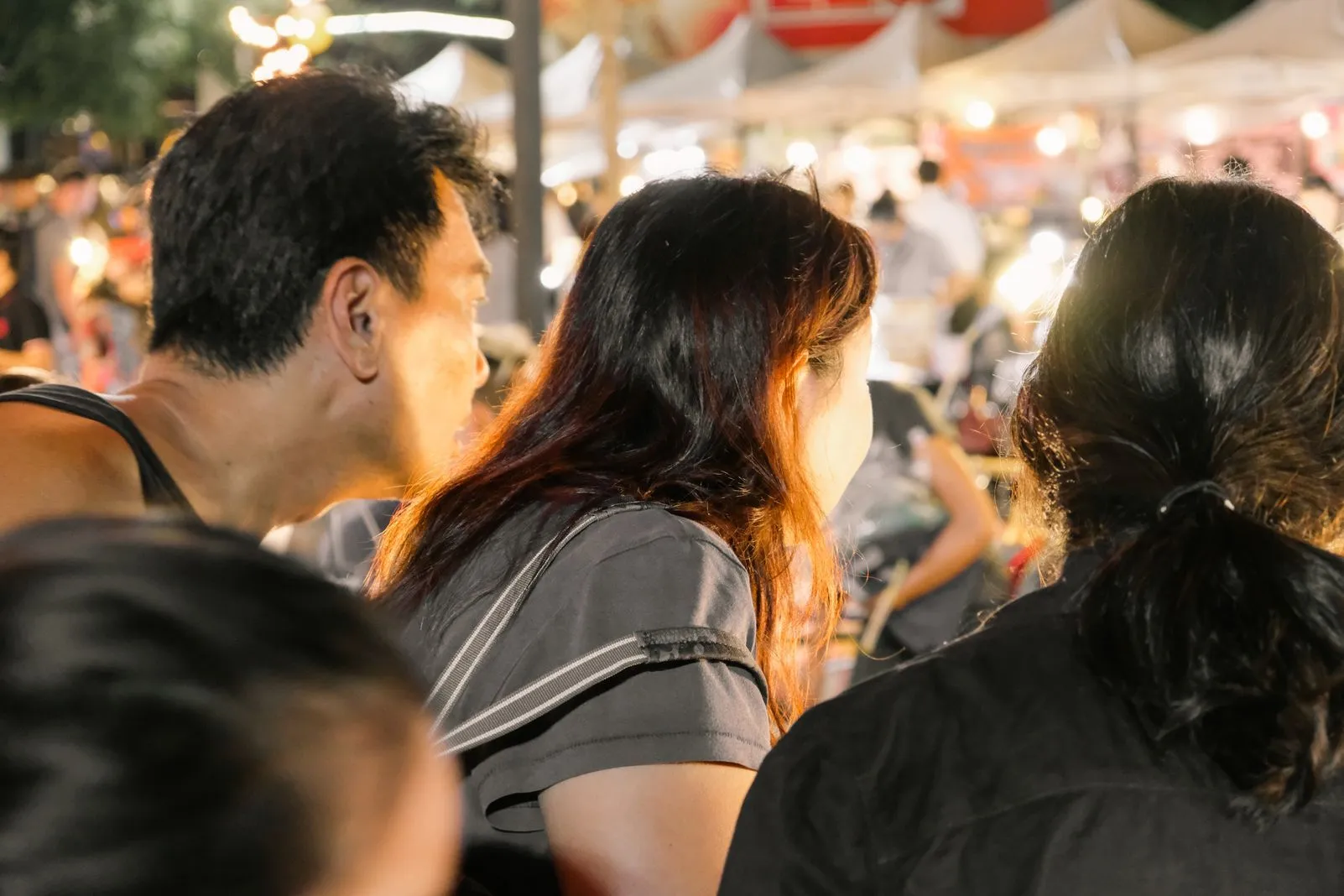Three people seen from behind amid a crowd at a night market