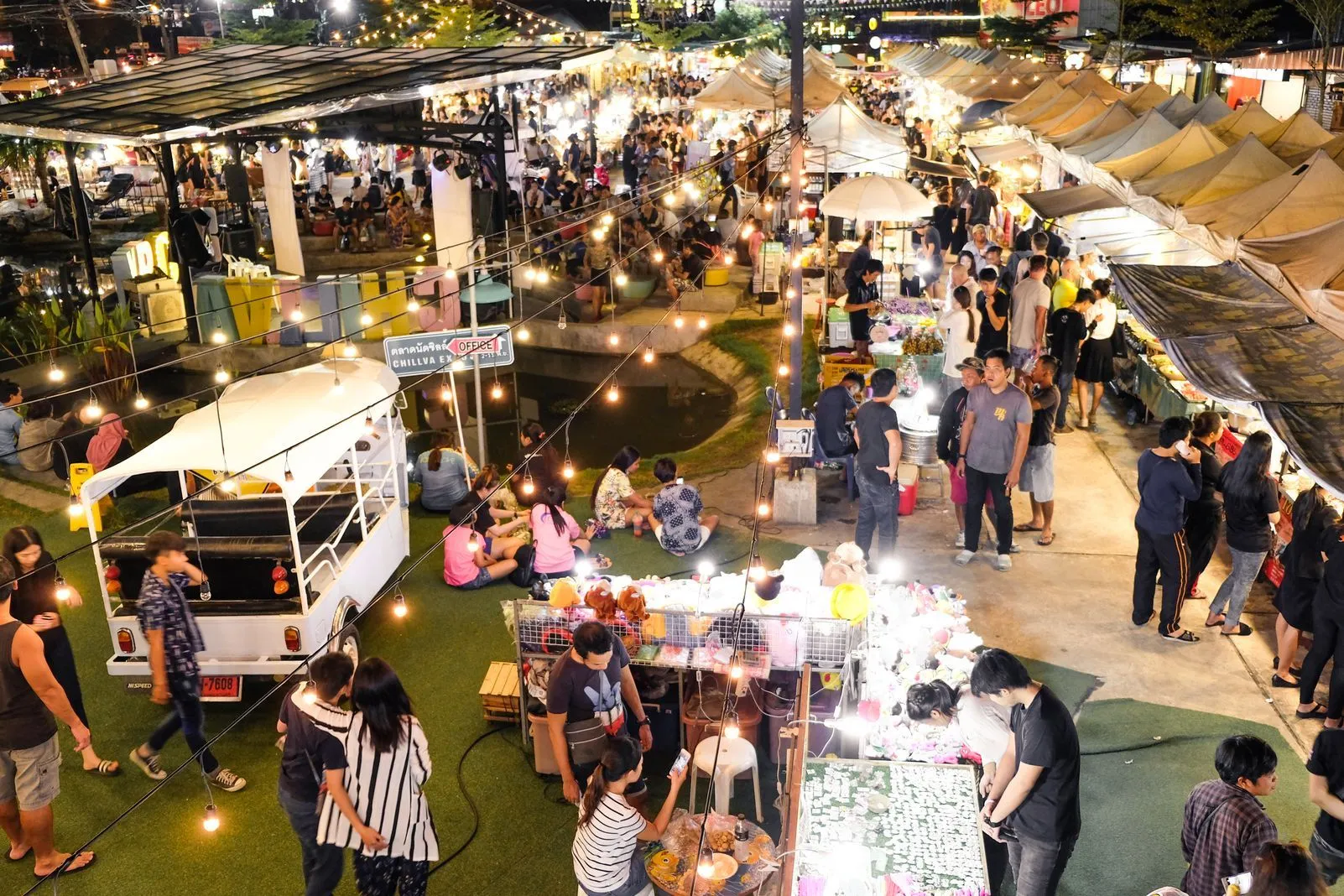 Aerial view of a bustling night market with food stalls, string lights, and crowds