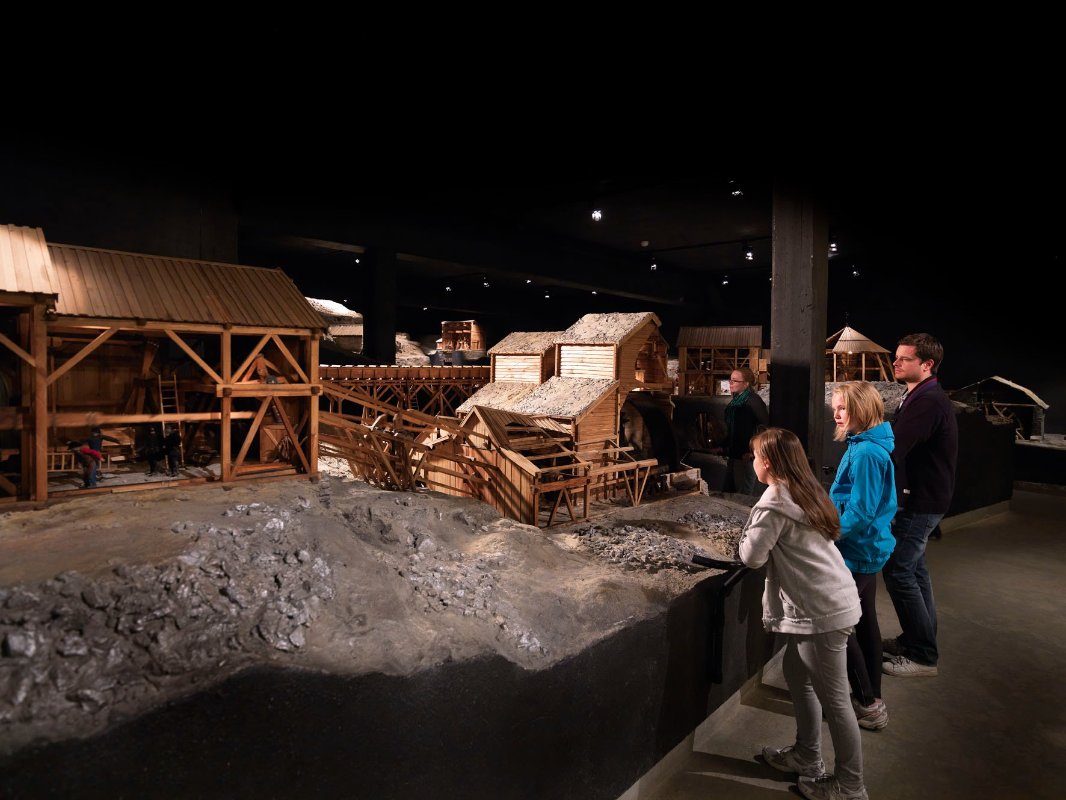 Besøkende studerer en modell som viser et historisk gruveanlegg i en museumsutstilling.