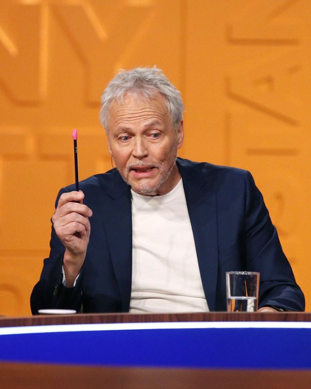 Tommy Sørbø - her i Nytt på Nytt. Sittende mann holder opp en blyant, ser ned med et engasjert uttrykk. Orasje bakgrunn