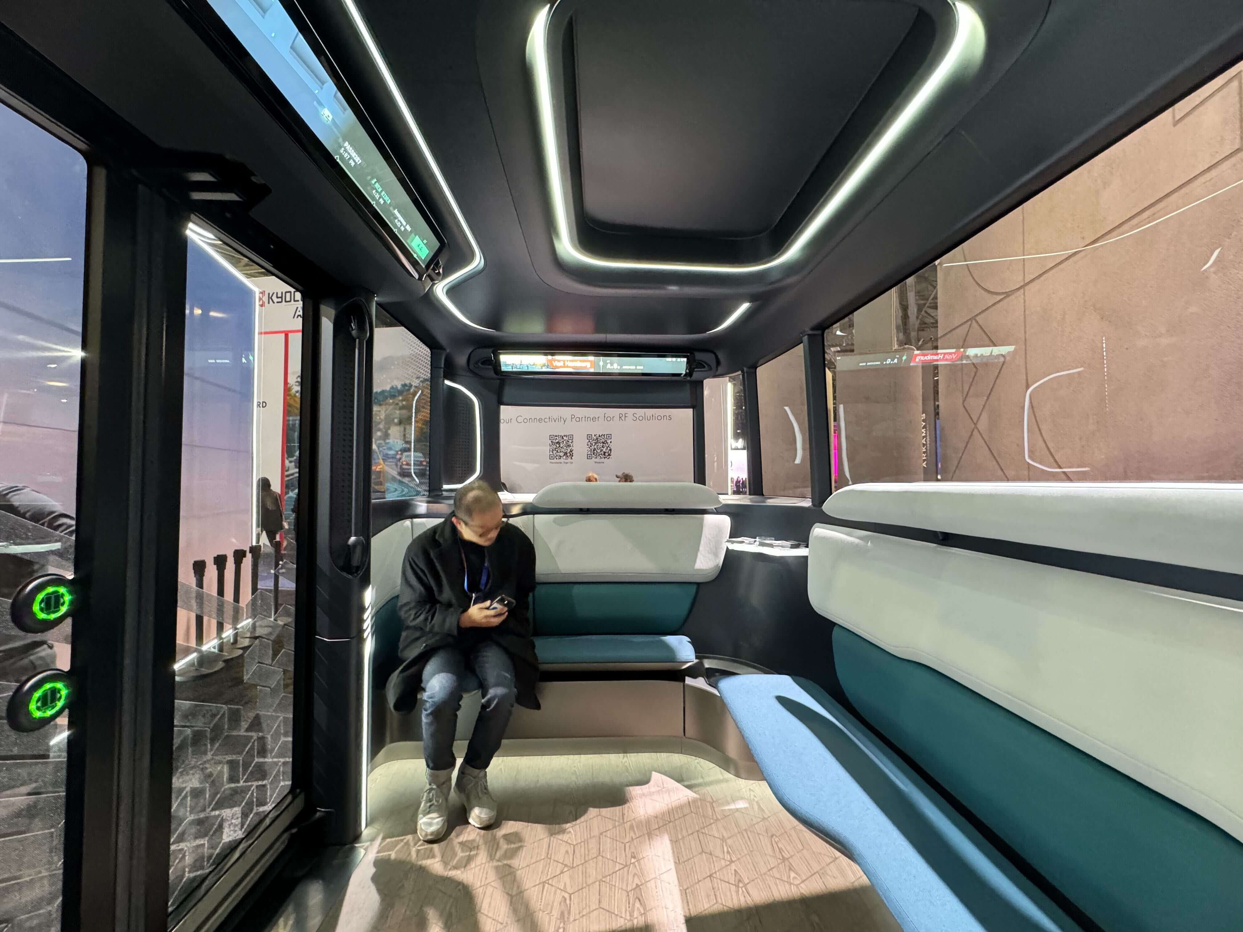 Interior of an autonomous shuttle: A person sits alone in a futuristic shuttle with sleek, modern interiors, blue and white seating, and ambient lighting.