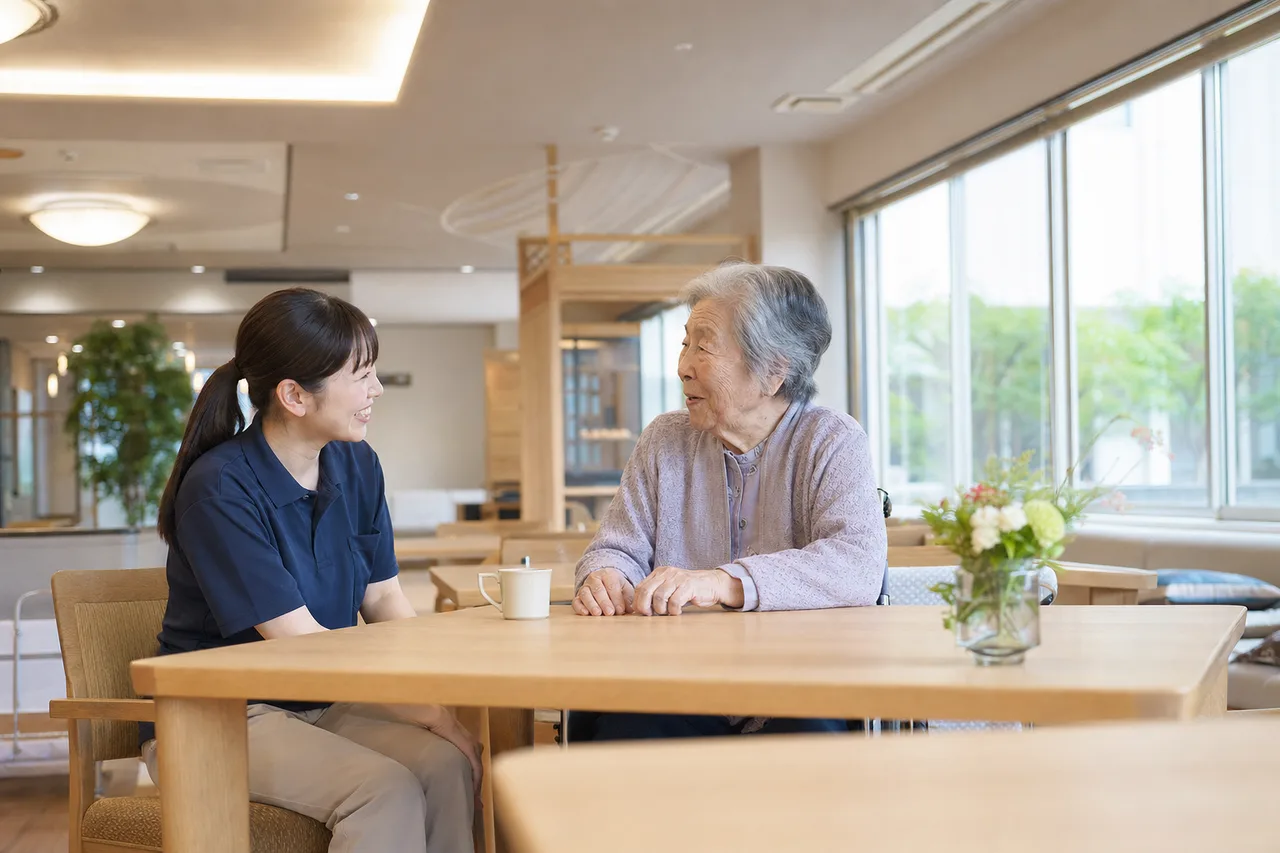 介護施設で会話する介護士と高齢者（パンフレット用）。介護施設で会話する介護士と高齢者をテーマに、パンフレット用として使いやすく構成した商用AI素材です。