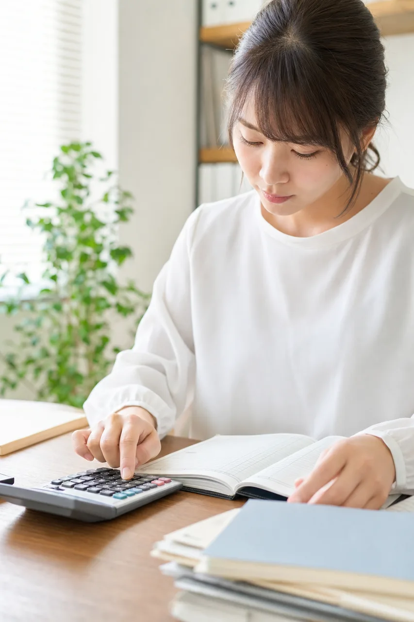 帳簿と電卓で決算を確認する経理担当者（縦型コンテンツ用）。帳簿と電卓で決算を確認する経理担当者をテーマに、縦型コンテンツ用として使いやすく構成した商用AI素材です。