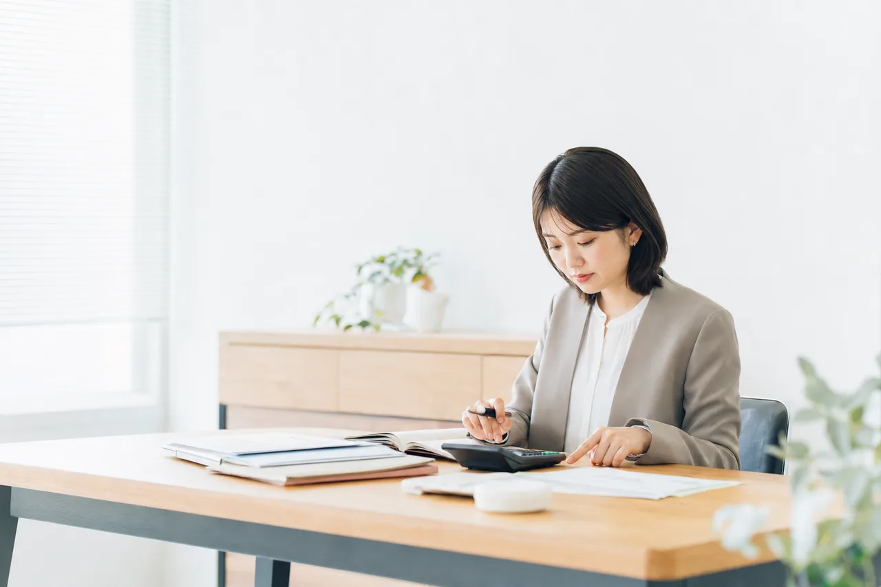 帳簿と電卓で決算を確認する経理担当者（サービス紹介用）。帳簿と電卓で決算を確認する経理担当者をテーマに、サービス紹介用として使いやすく構成した商用AI素材です。