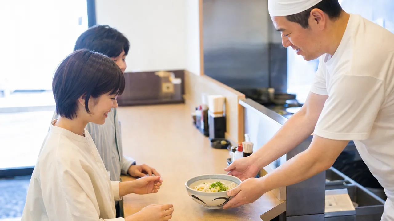 うどんを楽しむ日本人（横長・コピースペース）。うどん、麺料理、和食、飲食店の記事に使える素材です。