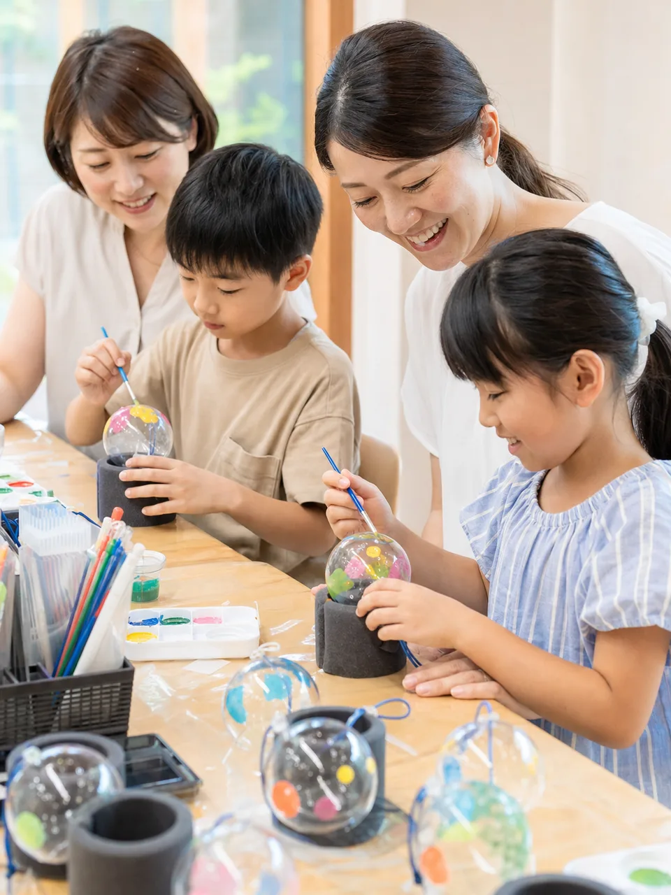 風鈴の絵付けを楽しむ日本人（自然な縦位置写真）。風鈴絵付け、風鈴作り、夏の工作、伝統工芸体験の記事や案内に使える商用素材です。
