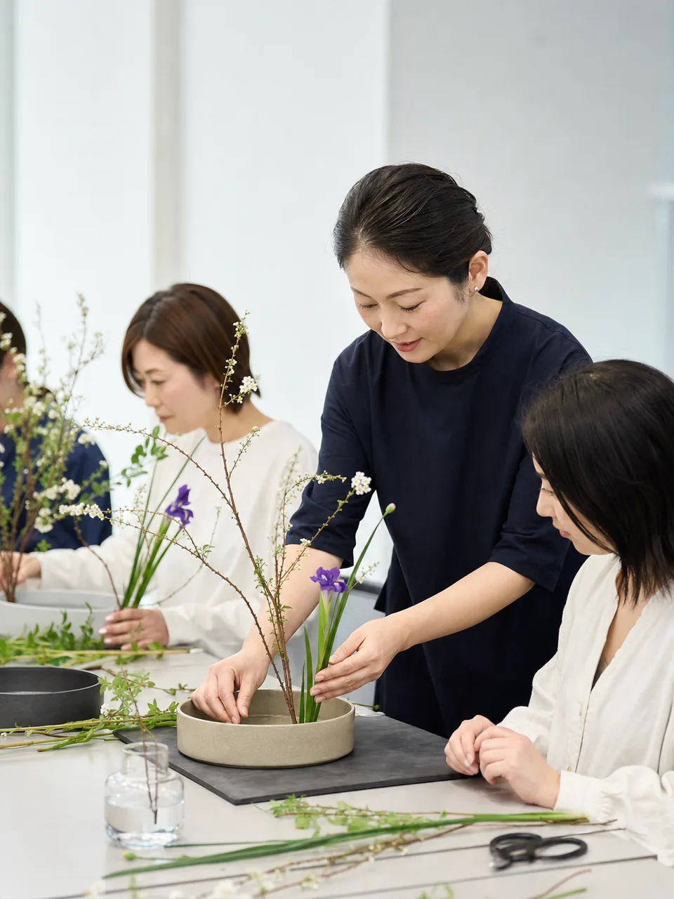 生け花を学ぶ日本人（自然な縦位置写真）。生け花、華道、花の教室、伝統文化の記事や案内に使える商用素材です。