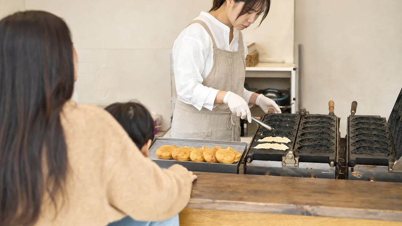 たい焼きを焼く日本人店員（横長・コピースペース）。たい焼き、和菓子、商店街、食べ歩きの記事向け素材です。
