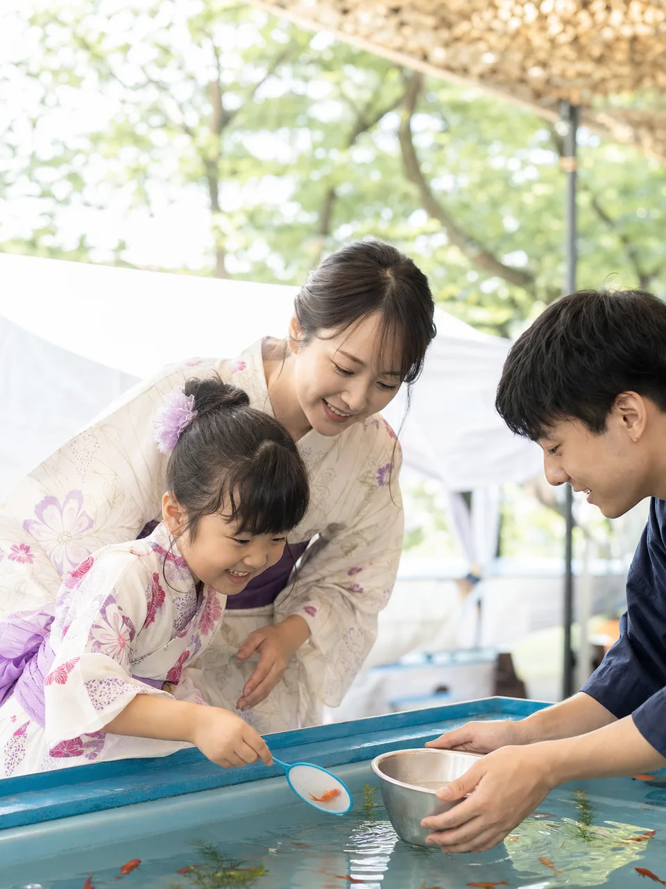 金魚すくいを楽しむ日本人親子（自然な縦位置写真）。金魚すくい、夏祭り、親子、縁日の記事や案内に使える商用素材です。