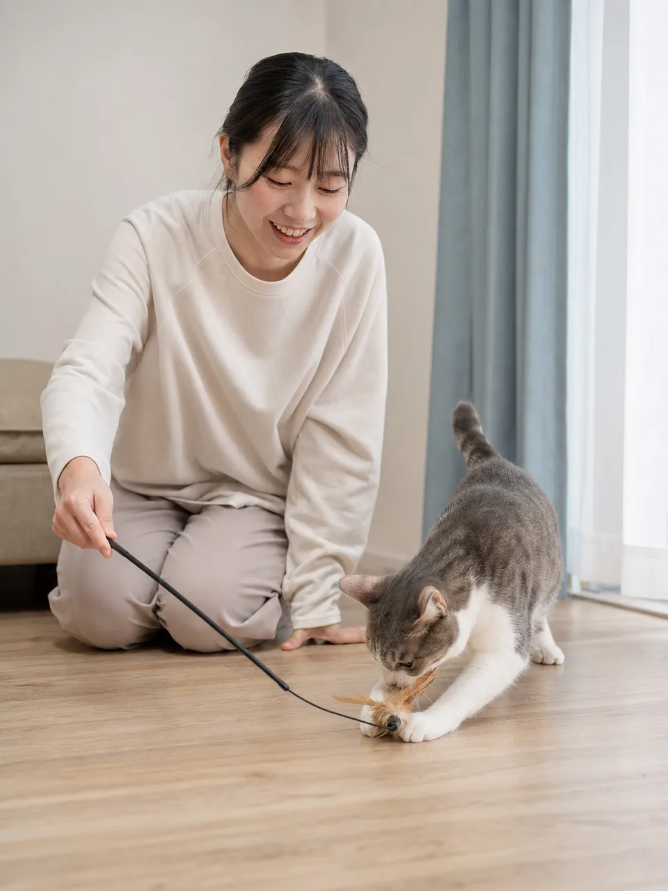 おもちゃで遊ぶ日本人と猫（自然な縦位置写真）。猫のおもちゃ、遊び、ペット、室内飼育の記事向け素材です。