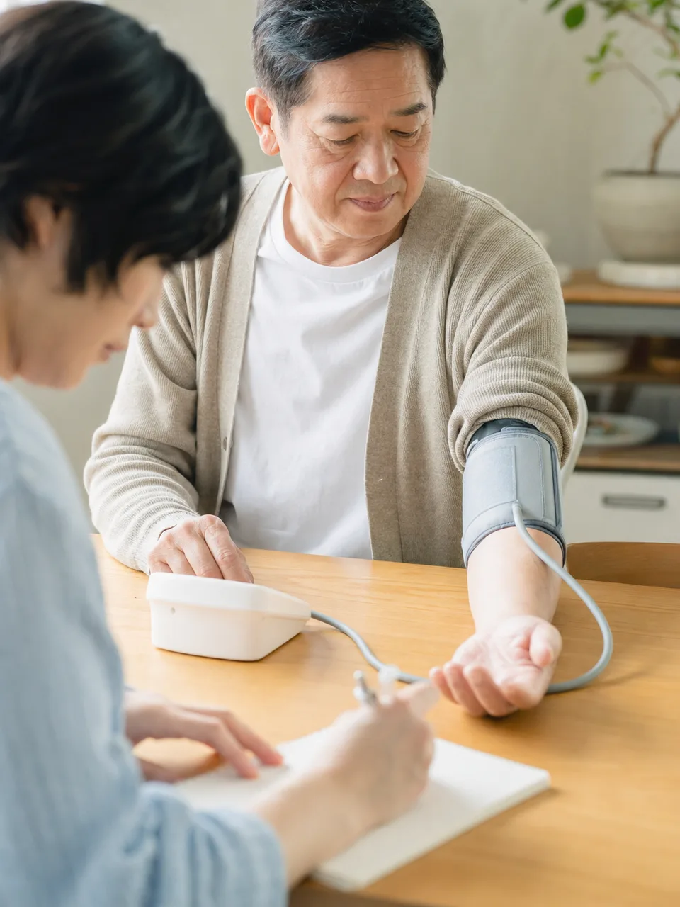 家庭で血圧を測る日本人（自然な縦位置写真）。高血圧、血圧測定、健康管理、家庭医療の記事向け素材です。