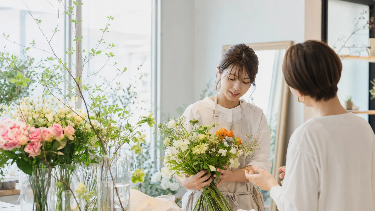 花を束ねる日本人の花屋スタッフ（横長・コピースペース）。花屋、フローリスト、花束、地域店舗の記事に使える素材です。
