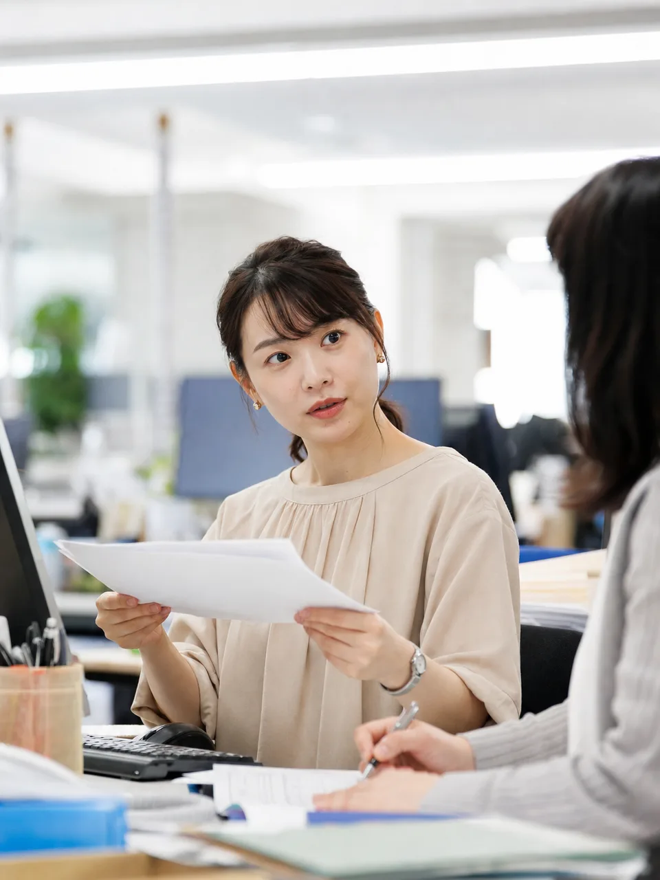 事務職として働く日本人会社員（自然な縦位置写真）。事務職、オフィスワーク、書類整理、業務支援の記事向け素材です。
