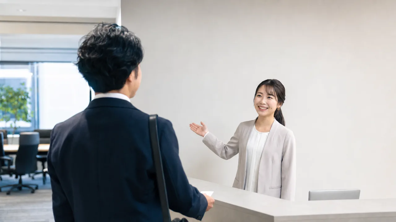 オフィスで案内する日本人受付スタッフ（横長・コピースペース）。受付、来客対応、オフィス、接客研修の記事向け素材です。