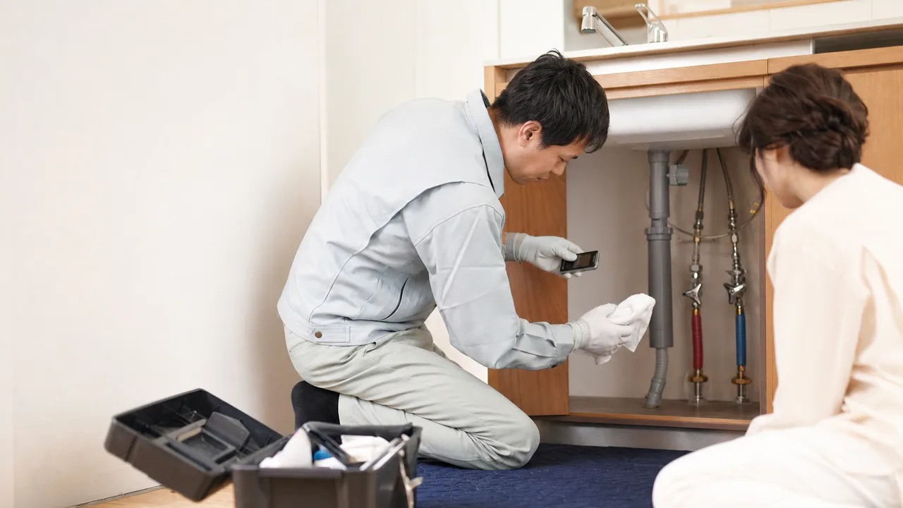 住宅の水漏れを確認する日本人配管技術者（横長・コピースペース）。水漏れ点検、配管、住宅修理、漏水の記事や案内に使える商用素材です。