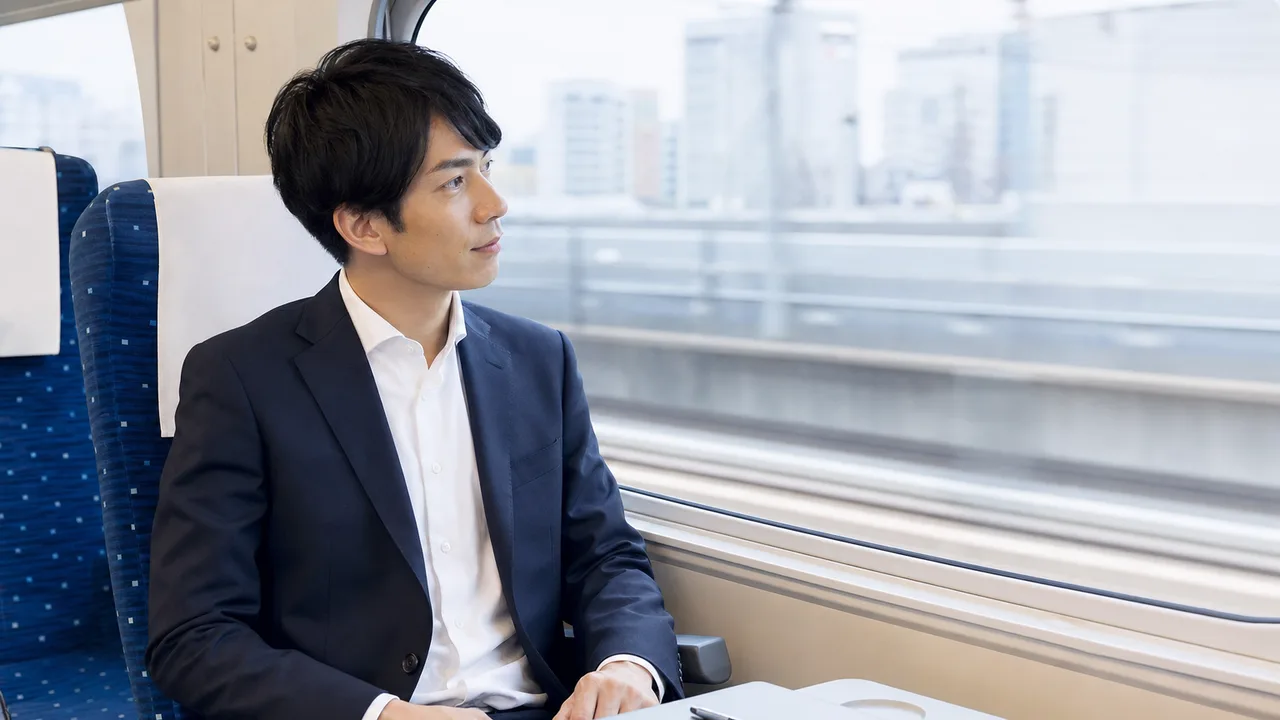 新幹線で出張する日本人会社員（横長・コピースペース）。新幹線、出張、鉄道、ビジネス旅行に使える移動中の素材です。