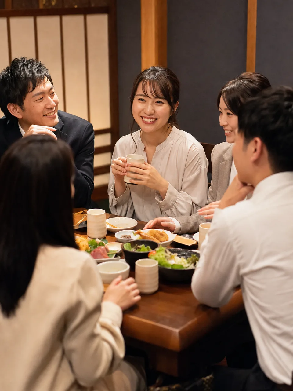 居酒屋で食事を楽しむ日本人同僚（自然な縦位置写真）。居酒屋、懇親会、外食、仕事帰りの交流を表現できる素材です。