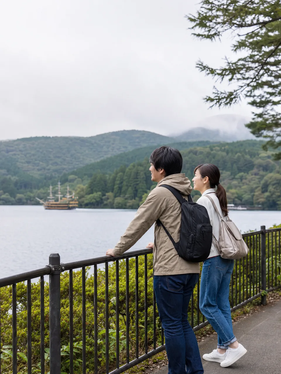 箱根の湖畔を歩く日本人旅行者（自然な縦位置写真）。箱根、温泉旅行、湖、国内旅行の記事に使える素材です。